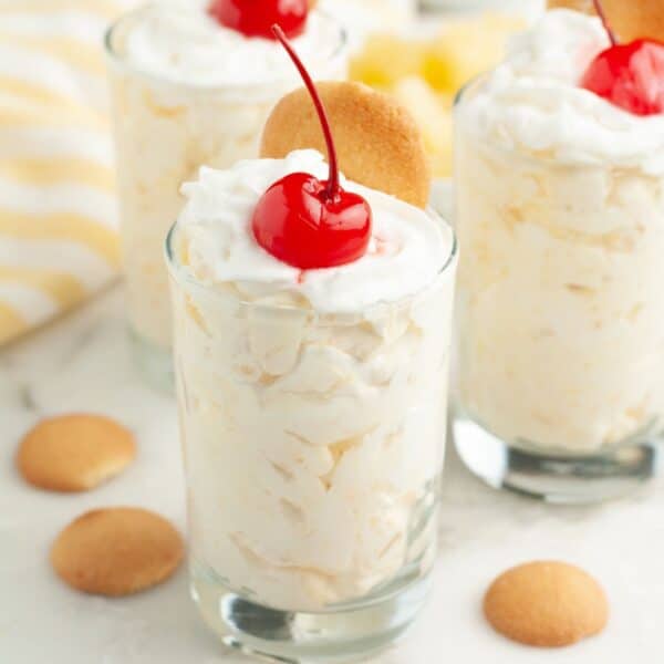Small glasses with pineapple pudding topped with whipped cream and cherry.