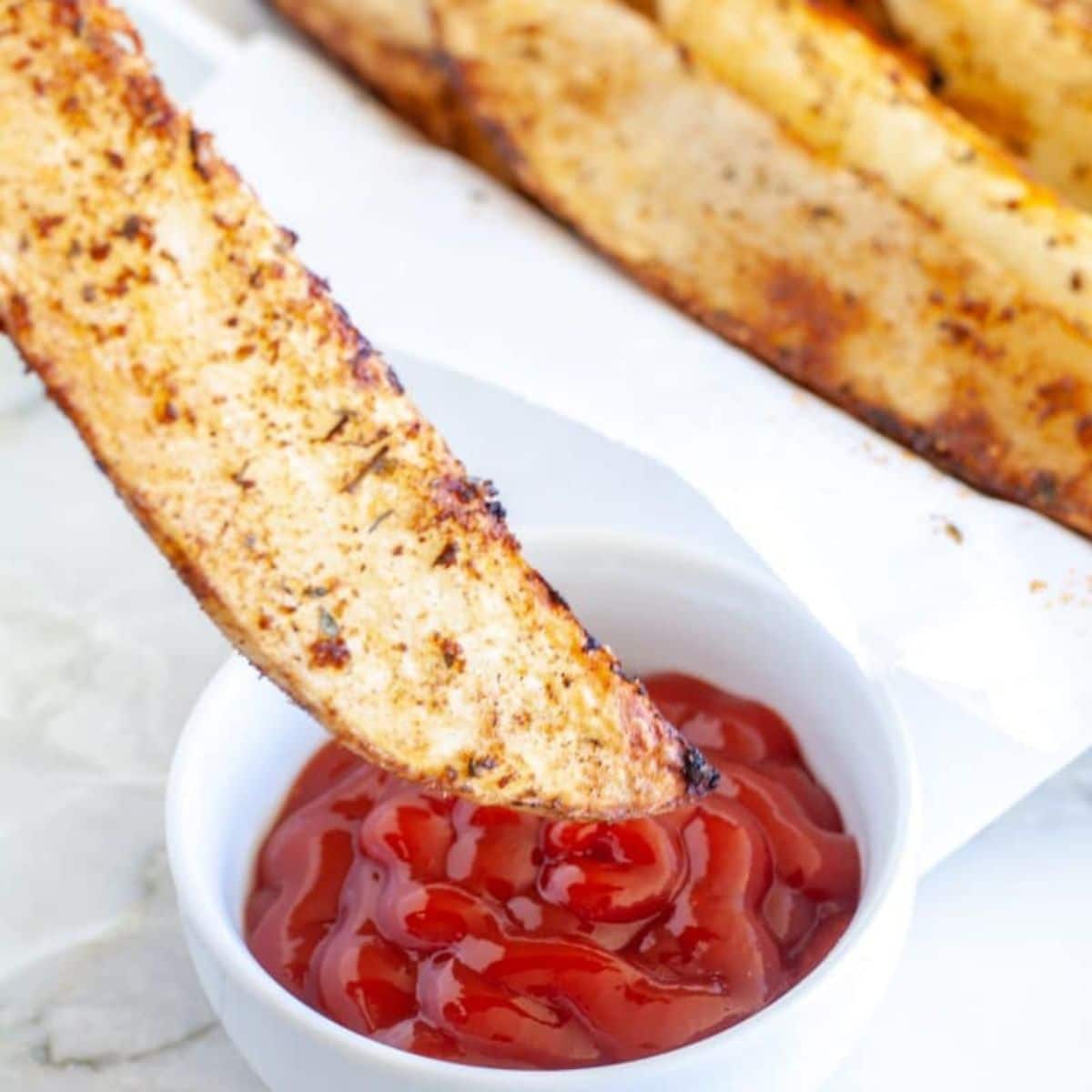 Potato wedge being dipped in ketchup.