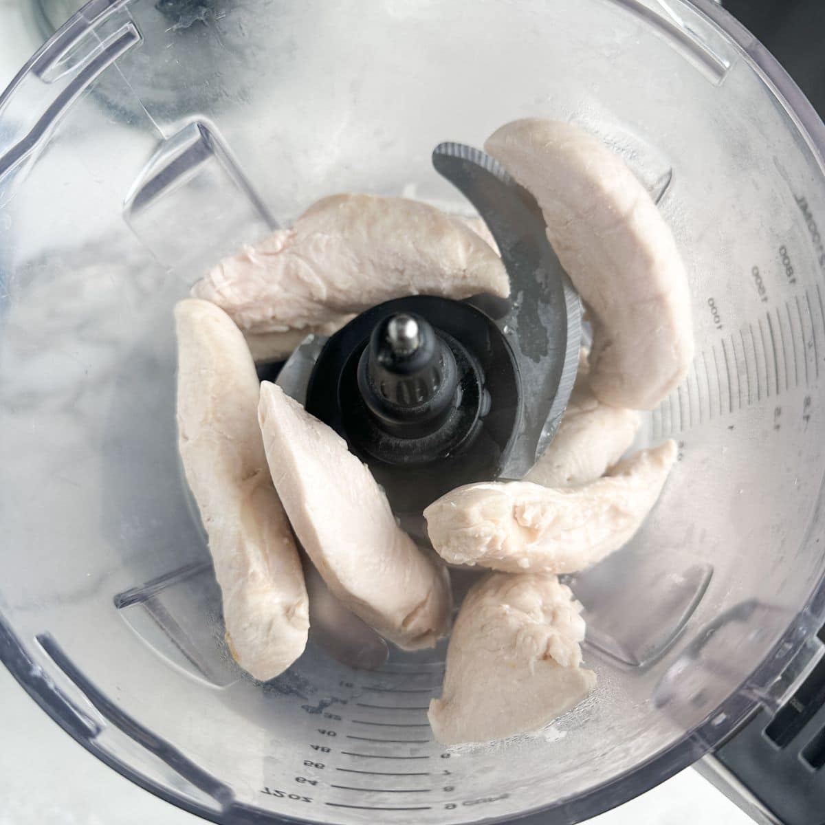 Food processor with cooked chicken tenderloins.