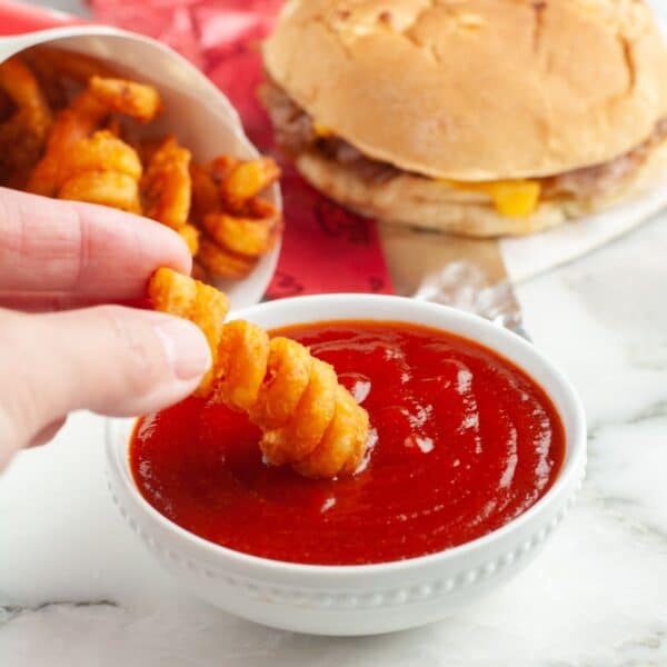 Bowl of red sauce with a curly fry dipping in the sauce.