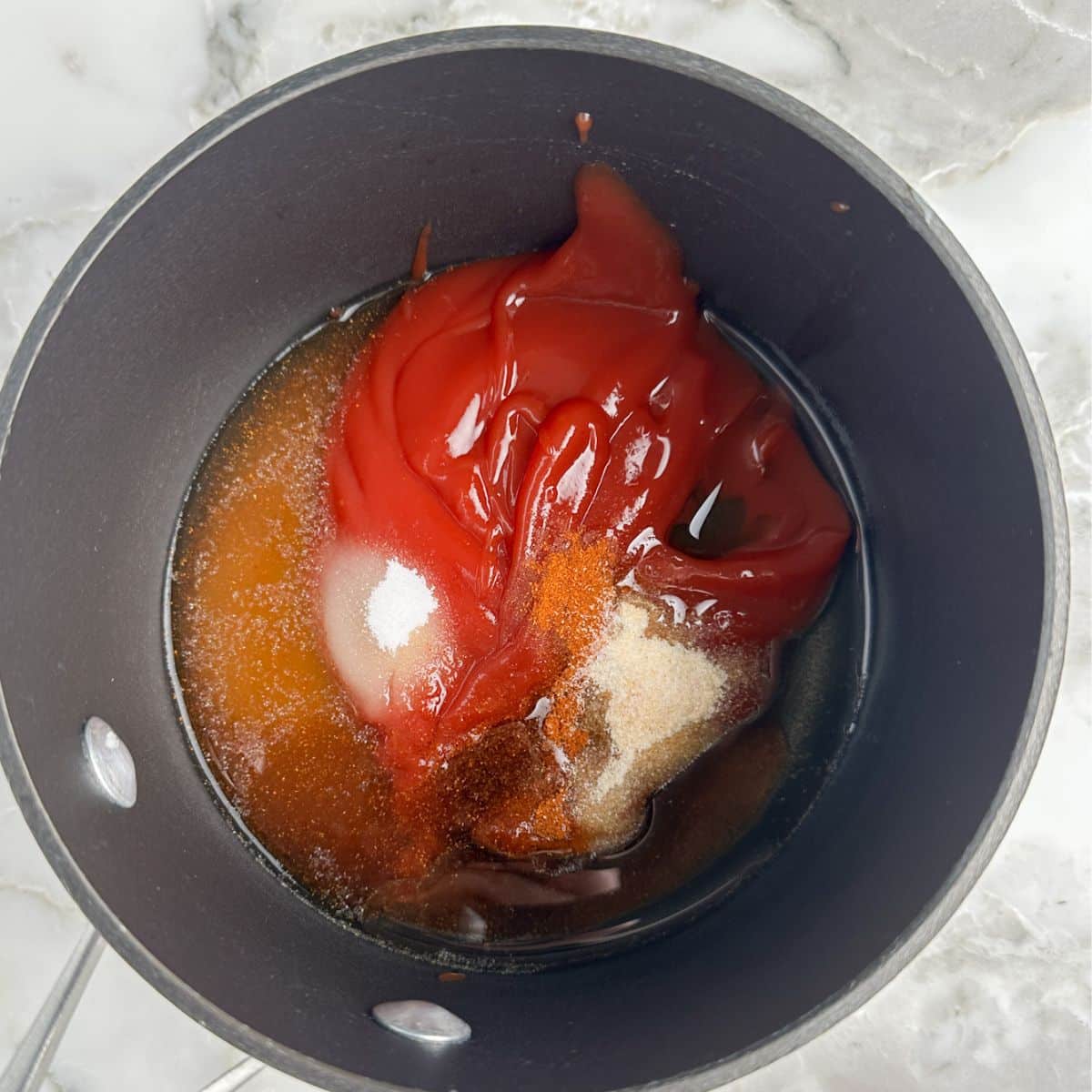 Saucepan with ketchup, seasonings, and oil. 