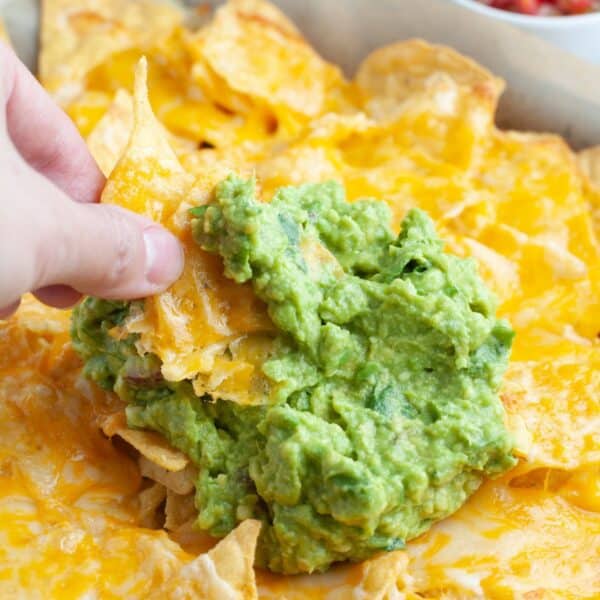 Hand holding nachos with guacamole.