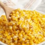Bowl of creamy corn with a wooden spoon.