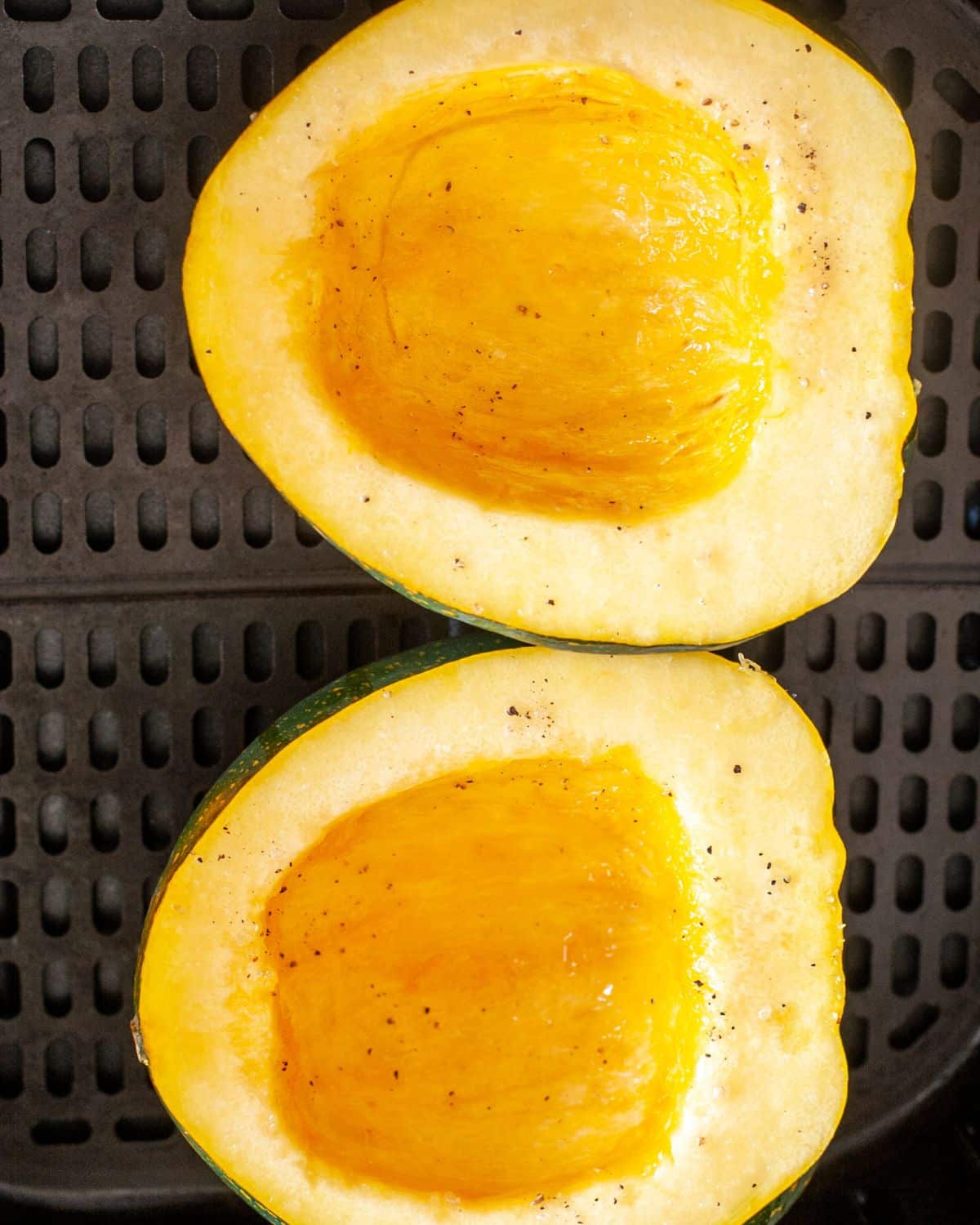 Halved acorn squash in an air fryer basket.