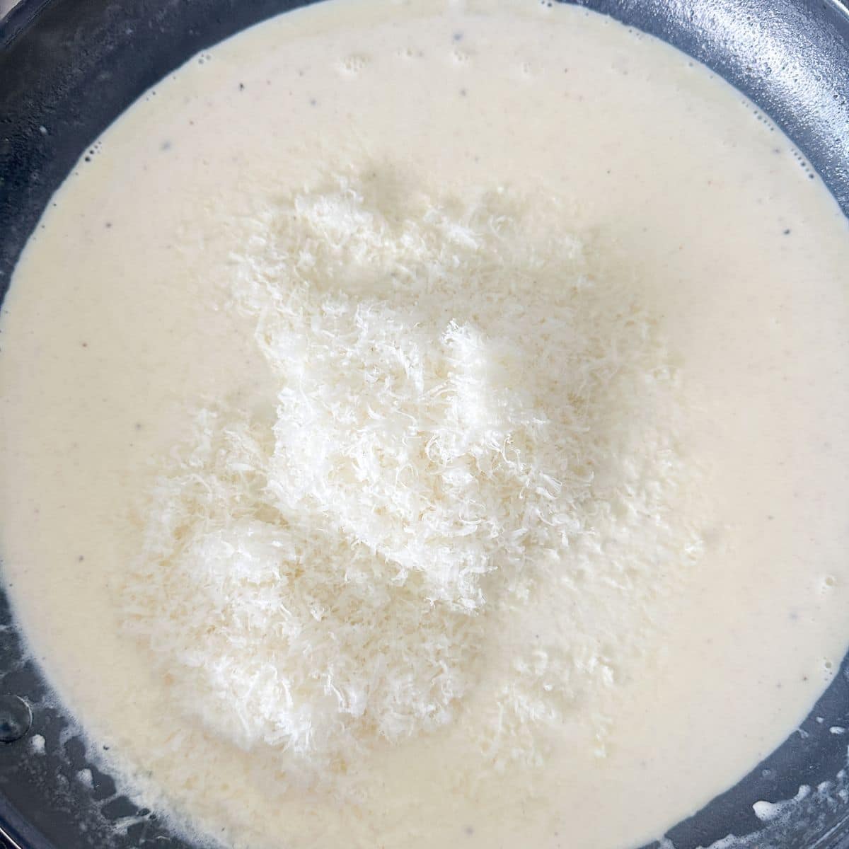 Skillet with alfredo sauce and shredded parmesan cheese.