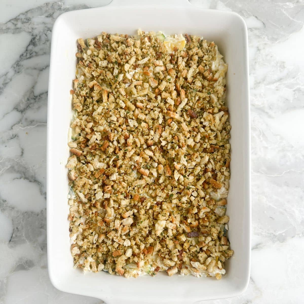 Casserole dish with cheesy chicken squash casserole topped with stuffing.