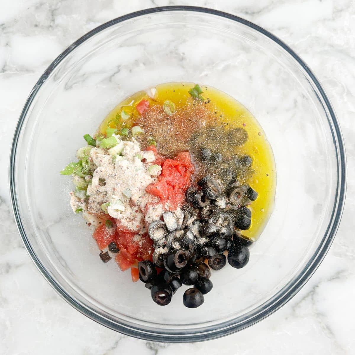 Bowl with black olives, diced tomatoes, seasoning, and oil.