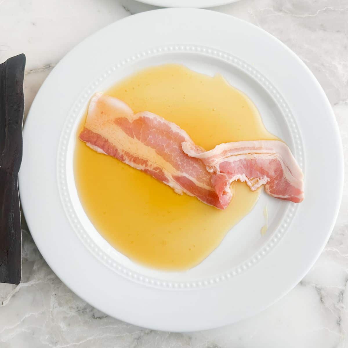 Plate with syrup and a piece of bacon.