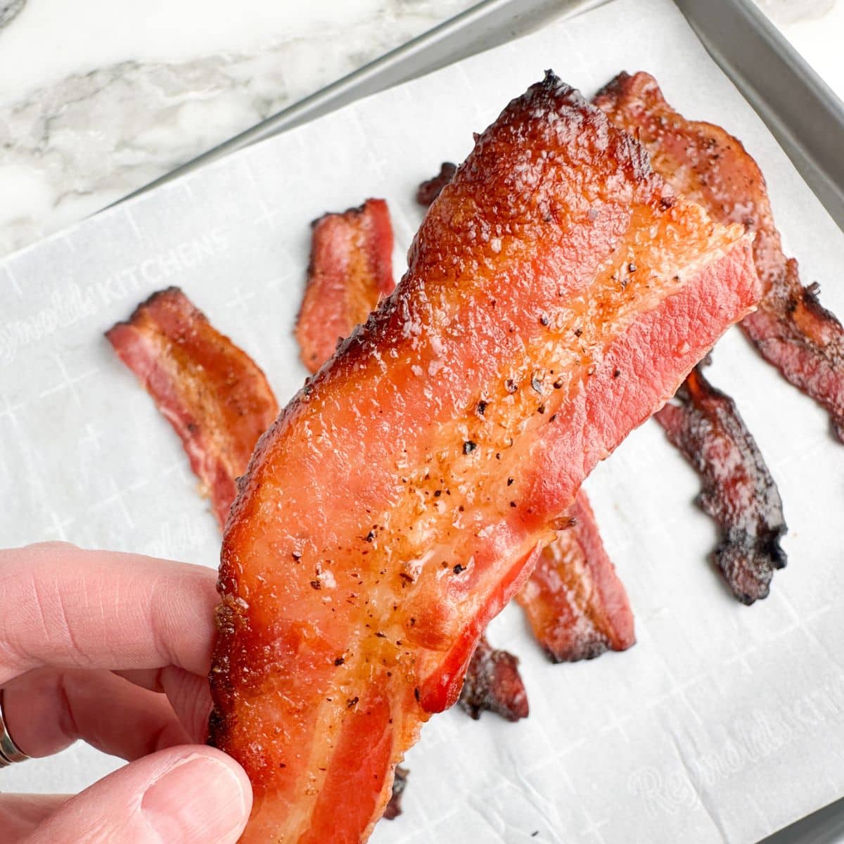 Hand holding a piece of cooked bacon.