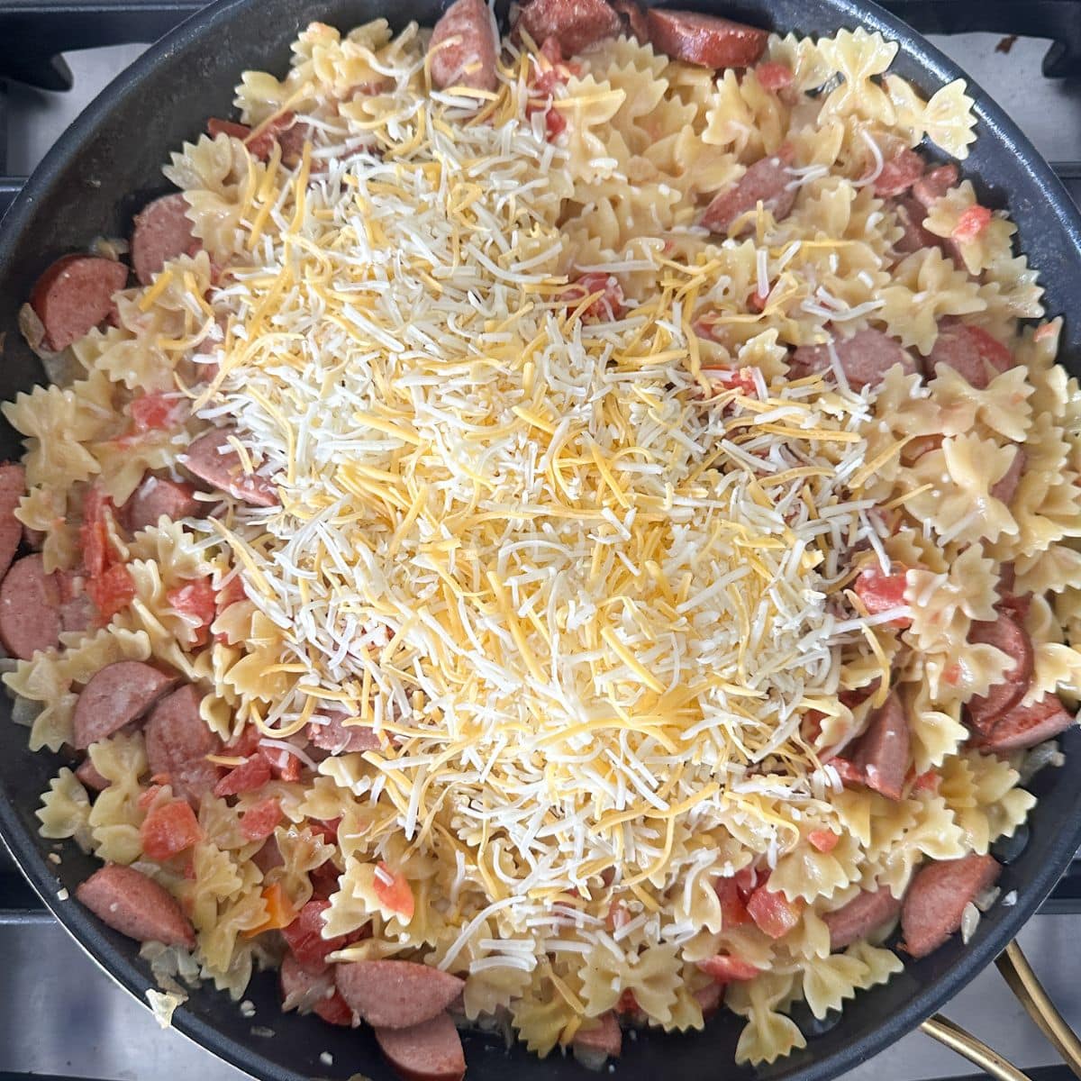 Skillet with kielbasa, pasta, and shredded cheese.
