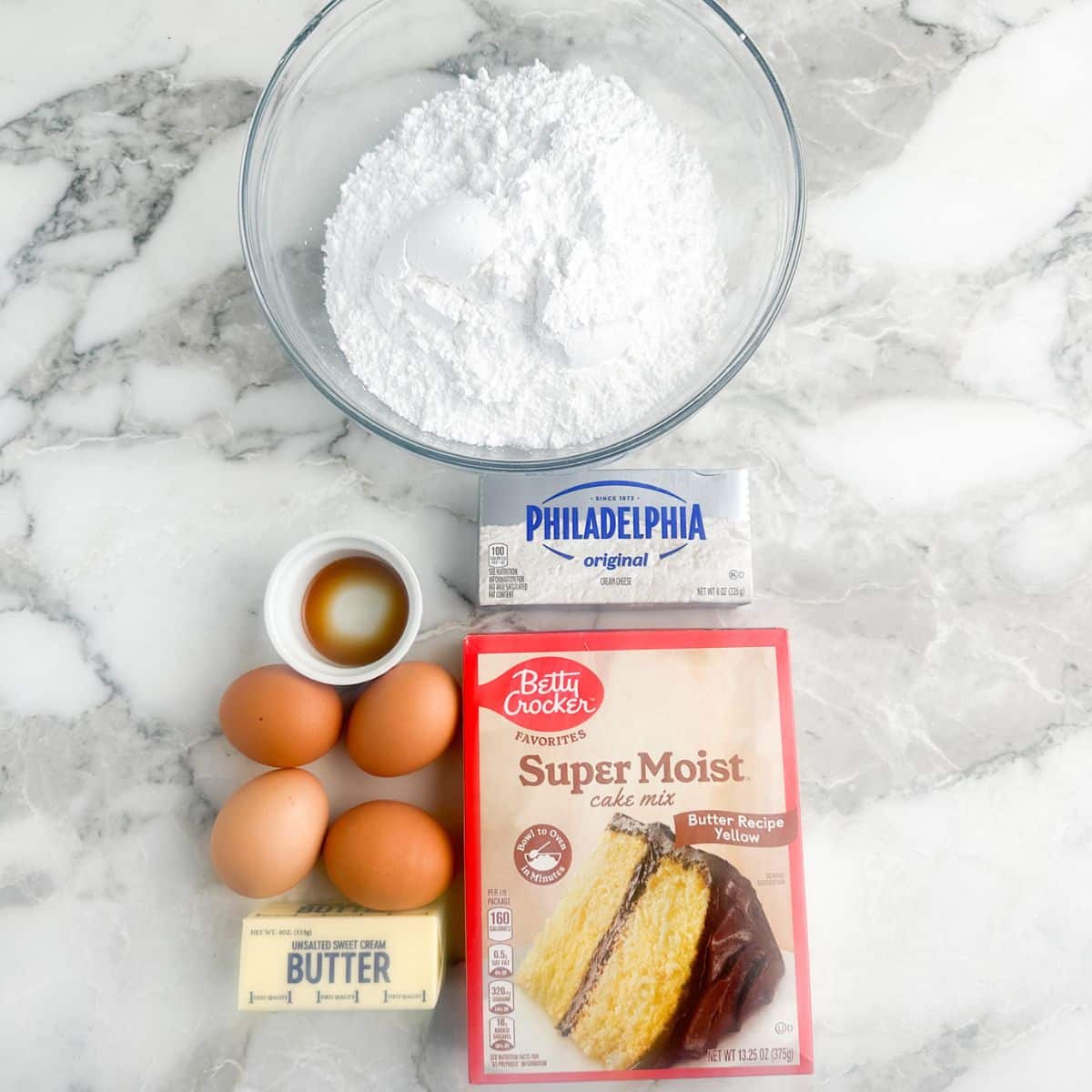 Bowl of powdered sugar, box of cake mix, eggs, butter, and cream cheese.