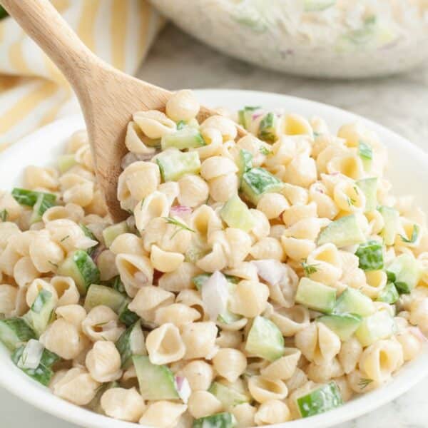 Bowl of cucumber pasta salad with a wooden spoon.