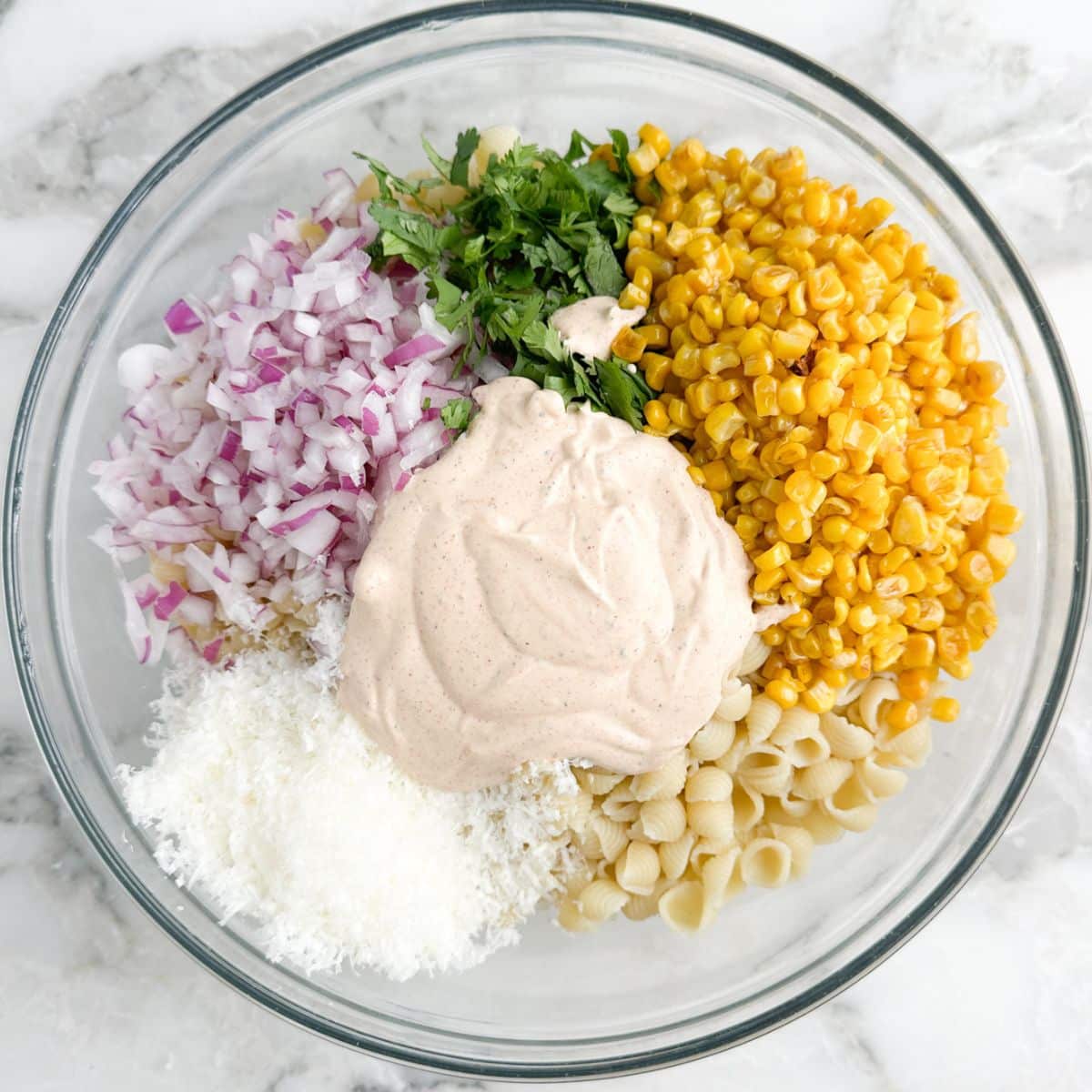 Bowl of pasta, corn, cilantro, onions, cheese, and dressing.