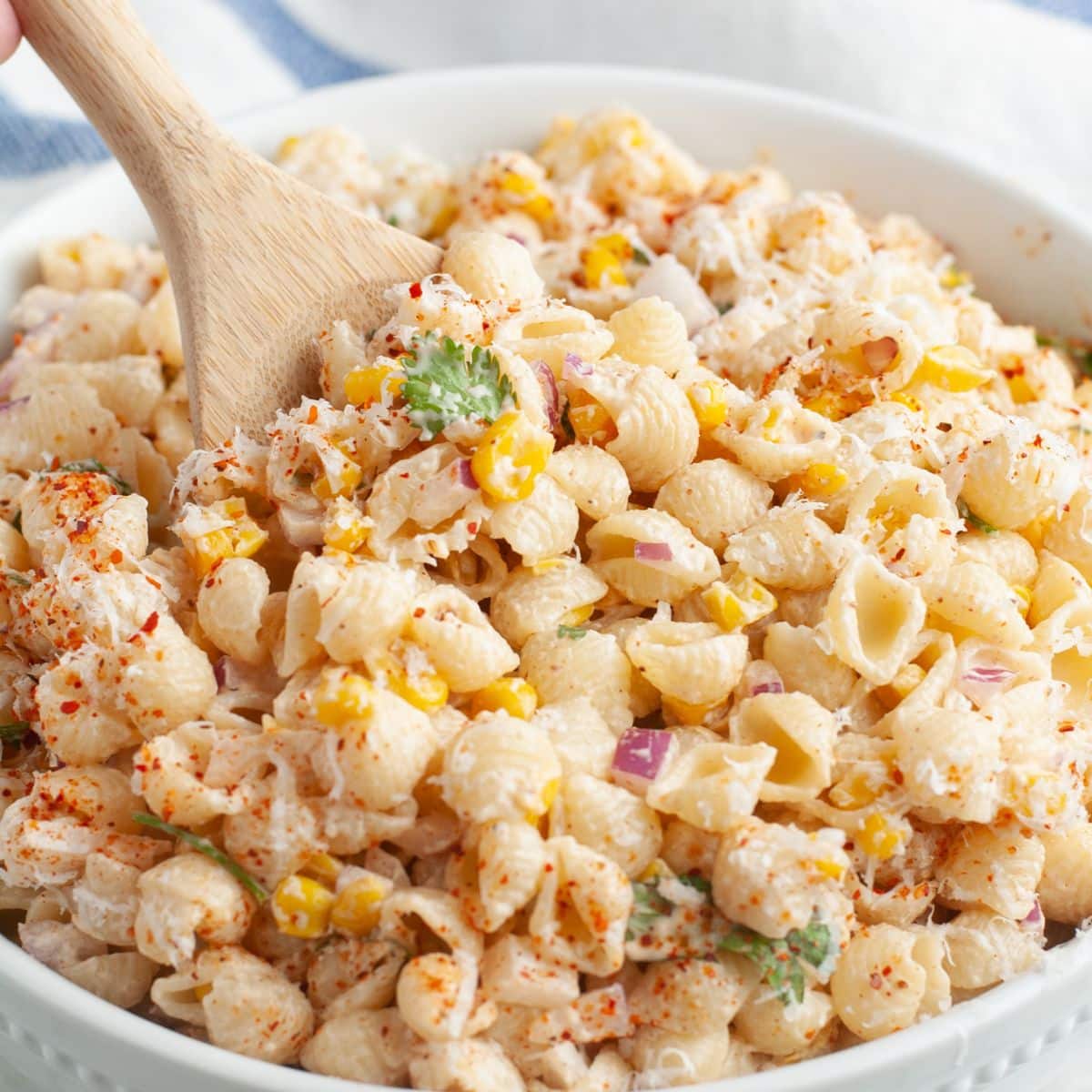 Bowl of elote pasta salad with a wooden spoon.