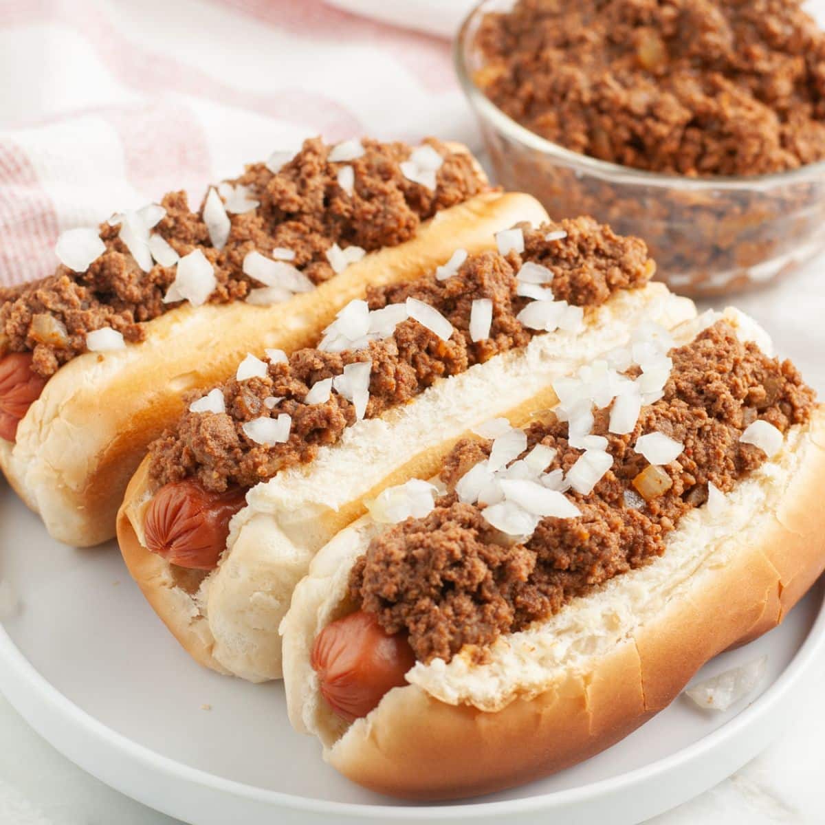 Plate of hot dogs topped with chili and onions.