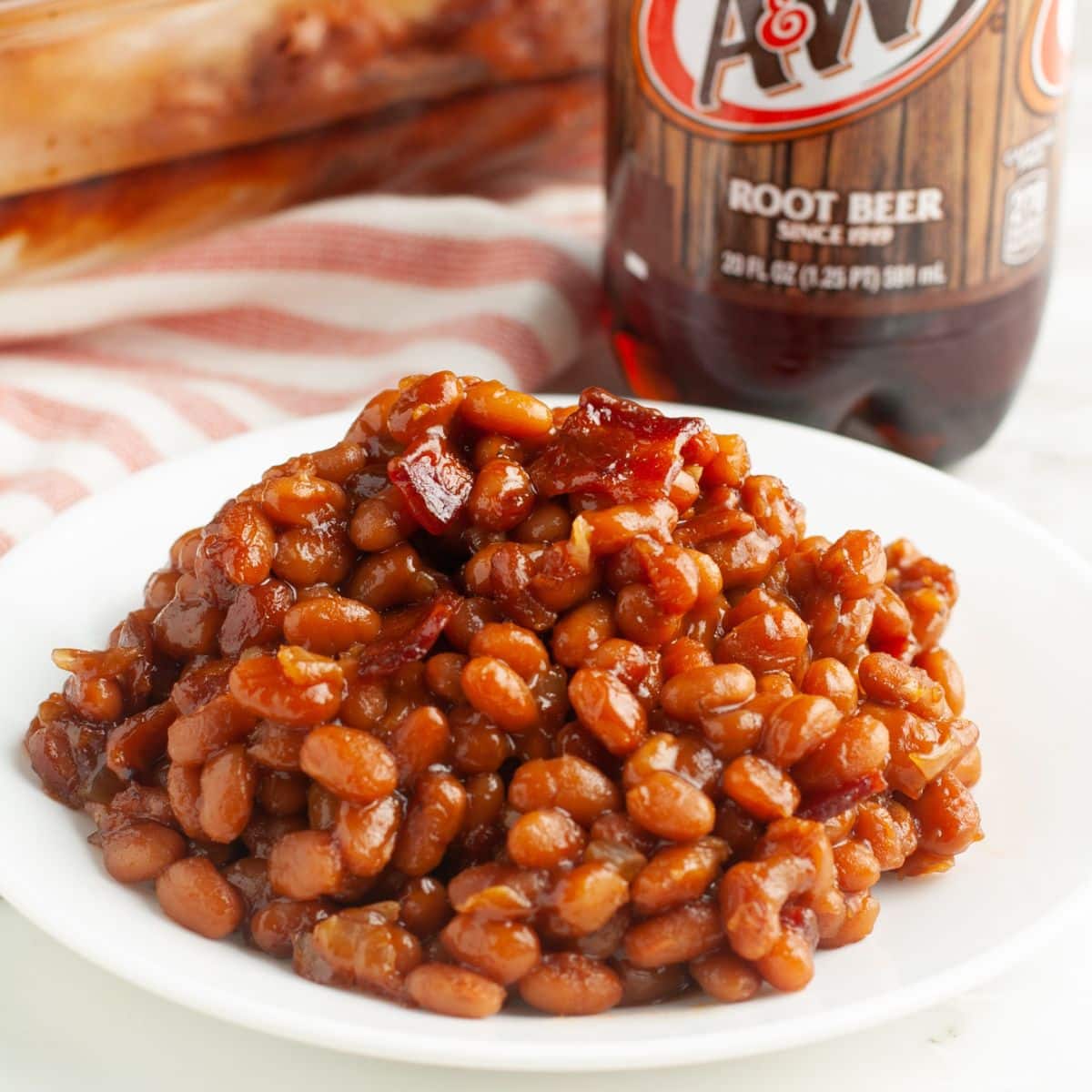 Plate of baked beans with a bottle of root beer.