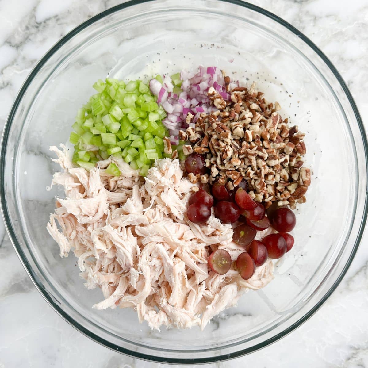 Bowl of shredded chicken, diced celery, pecans, grapes, and onions.