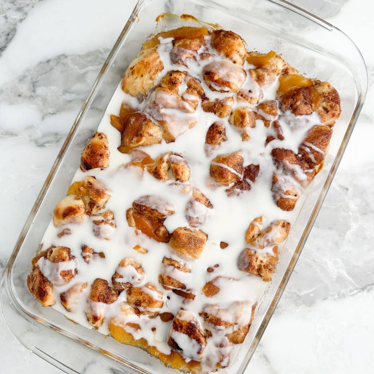Baked cinnamon roll peach cobbler with icing.
