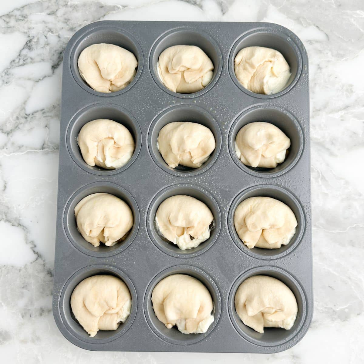 Muffin tin filled with uncooked mini peach crescent cheesecakes.