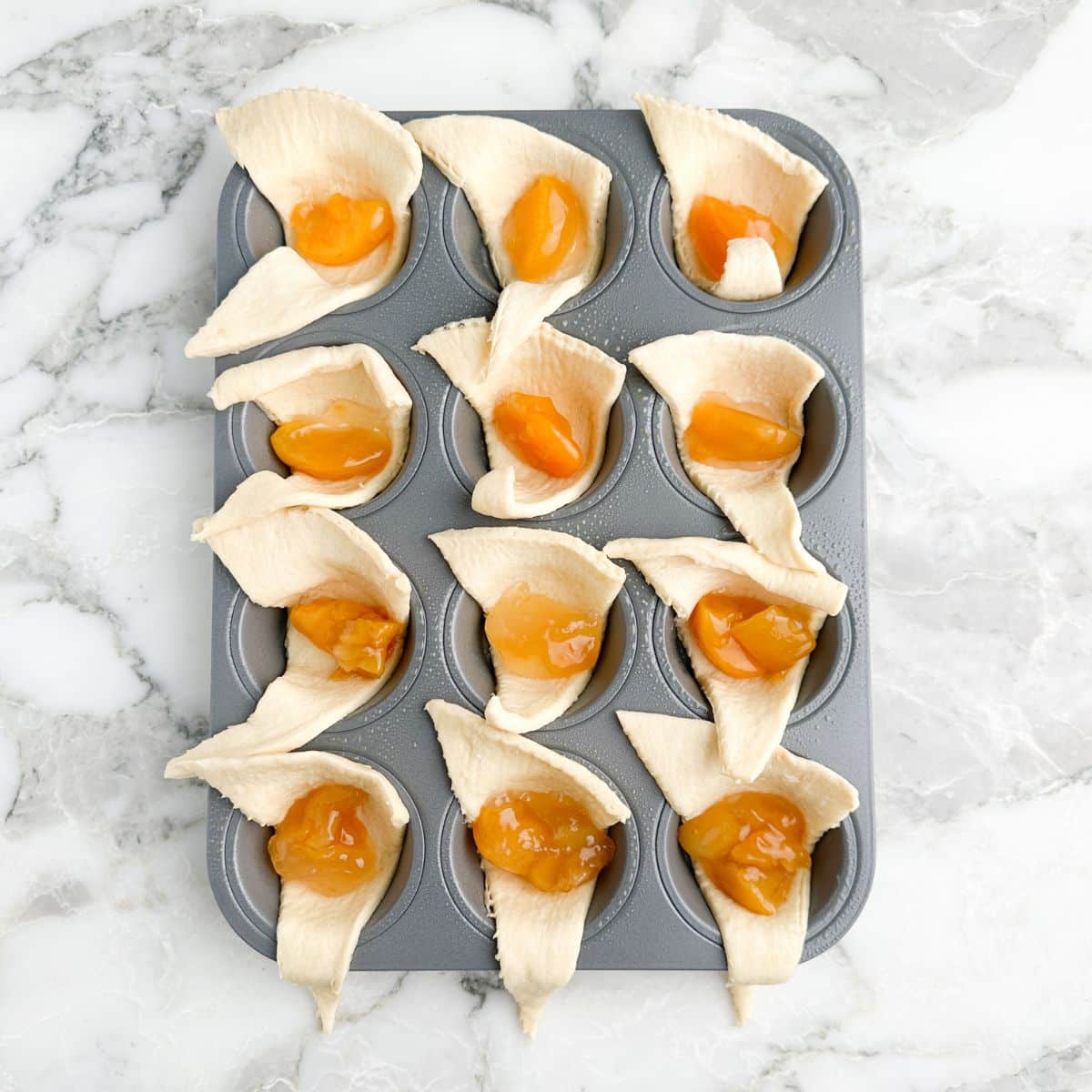 Muffin tin with crescent roll dough and peach pie filling.