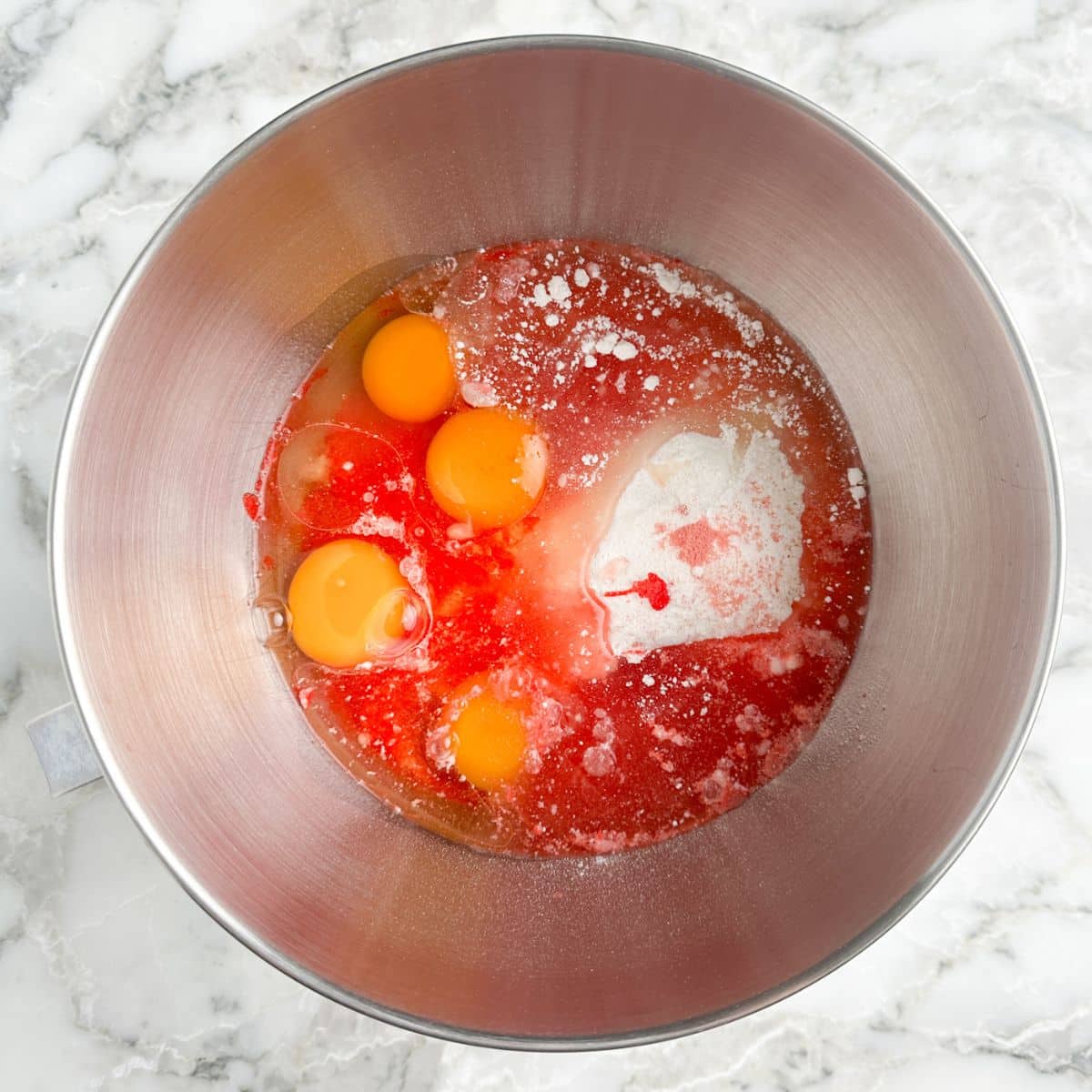 Mixing bowl with chopped strawberries, eggs, cake mix, and oil.