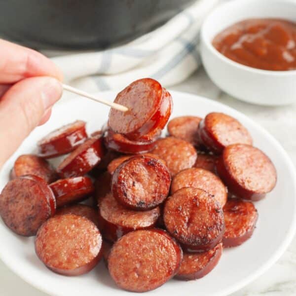 Plate of kielbasa rounds with a hand holding one on a toothpick.
