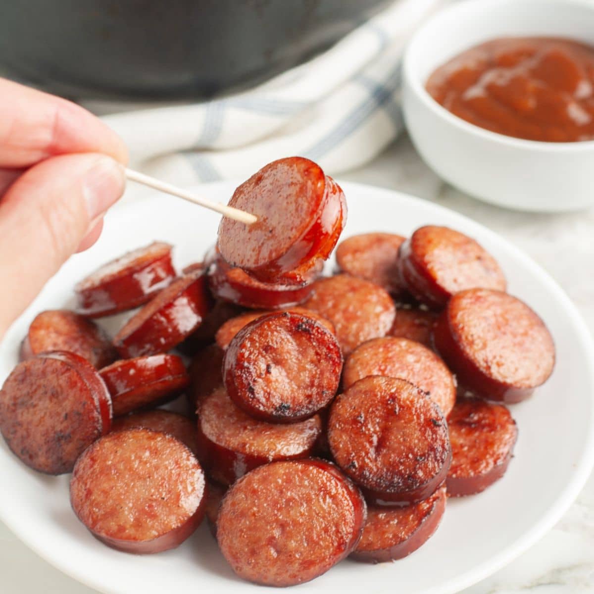 Plate of kielbasa rounds with a hand holding one on a toothpick.