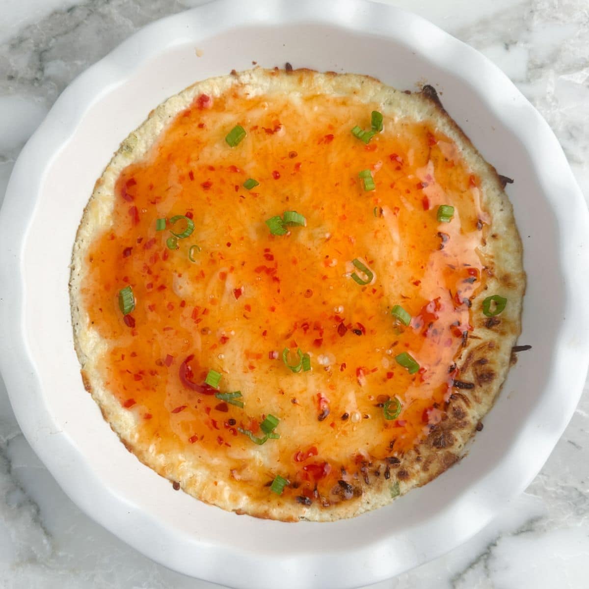Baking dish with crab rangoon dip topped with sweet chili sauce.