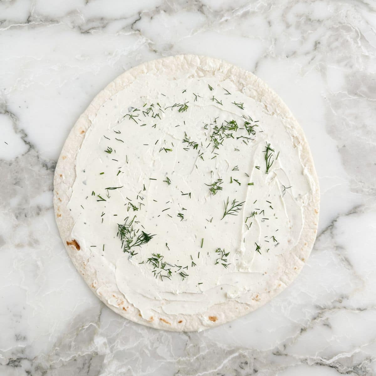Flat tortilla with cream cheese spread over it. 