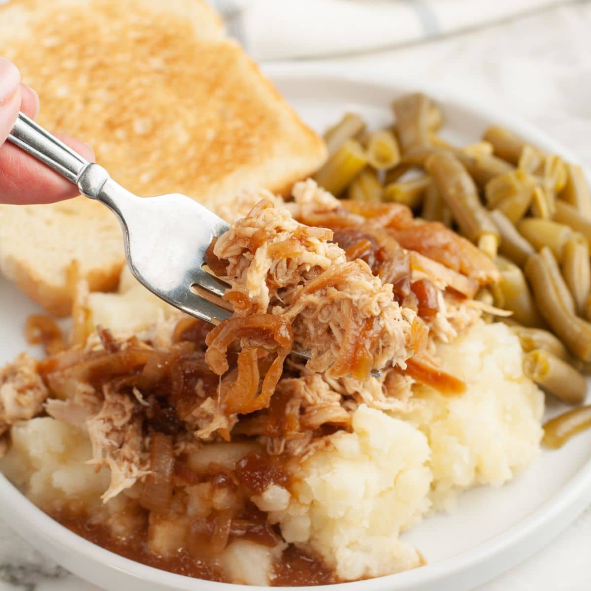 Fork holding shredded French onion chicken with mashed potatoes and green beans.