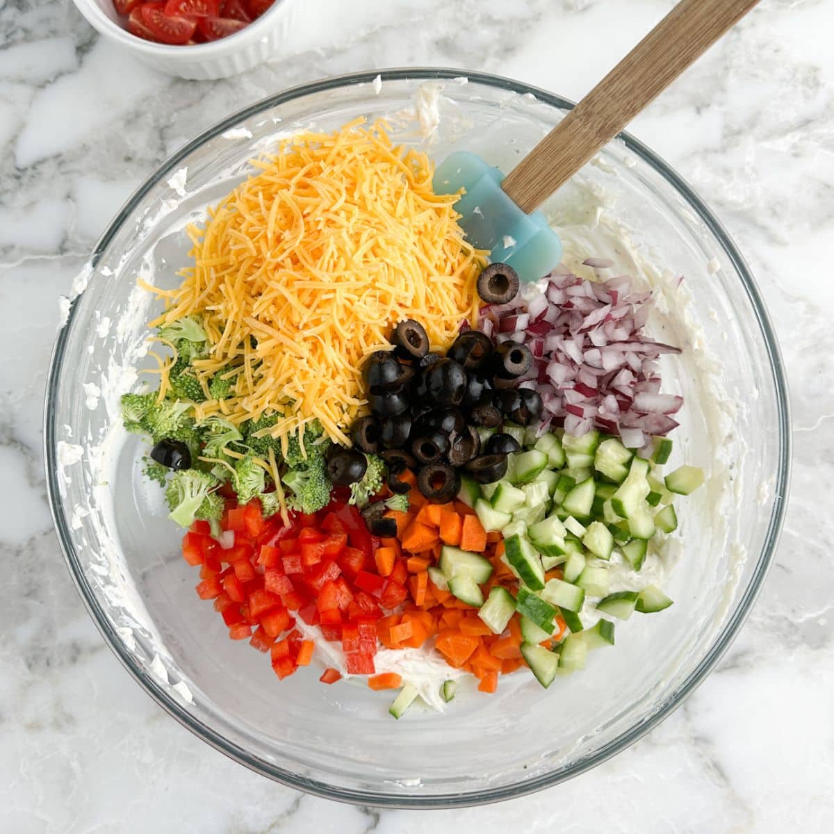 Bowl with shredded cheese, diced peppers, cucumbers, red onion, and broccoli.