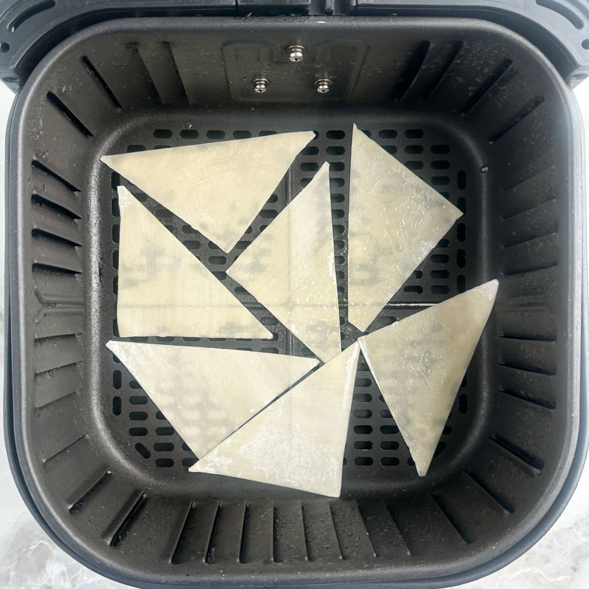 Air fryer basket with uncooked wonton wrappers.