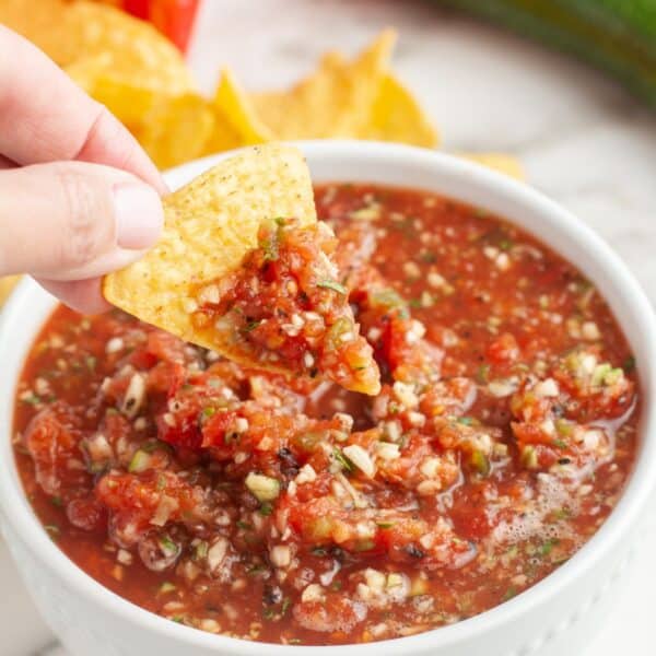 Bowl of salsa with a tortilla chip dipping into it.