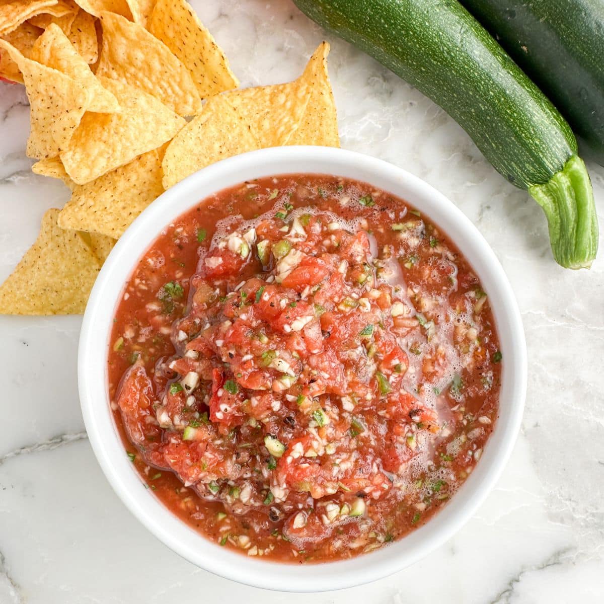 Bowl of zucchini salsa with tortilla chips and zucchini.