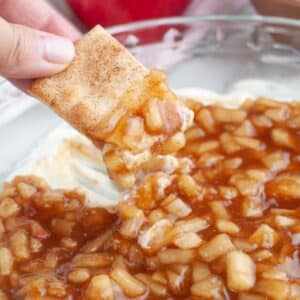 Hand holding a cinnamon cracker with apple pie dip.
