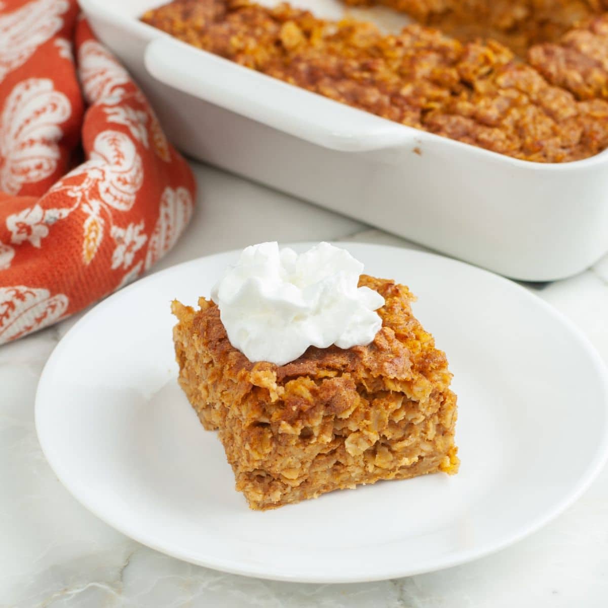 Plate with a piece of baked pumpkin oatmeal topped with whipped cream.