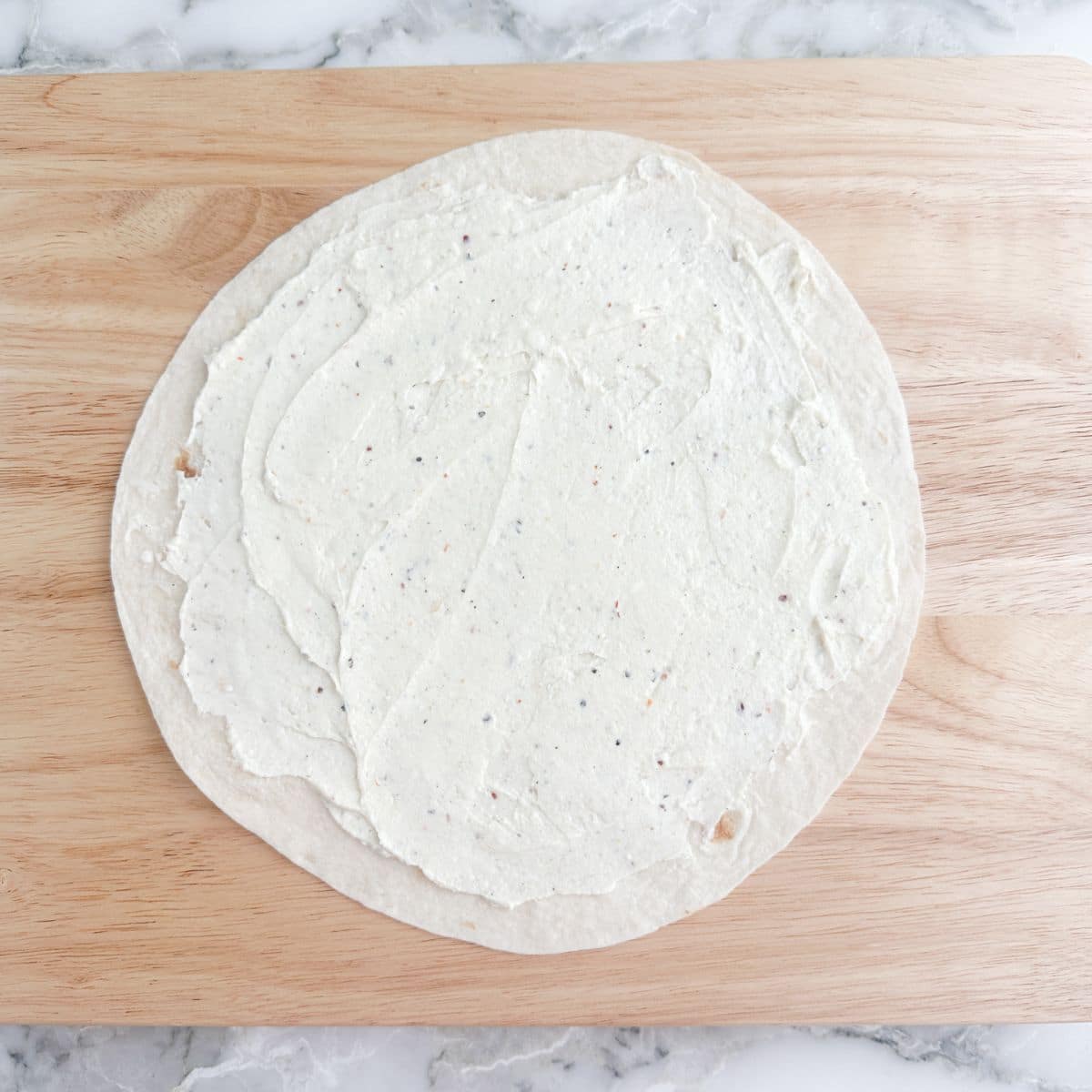 Tortilla topped with cream cheese spread on top.