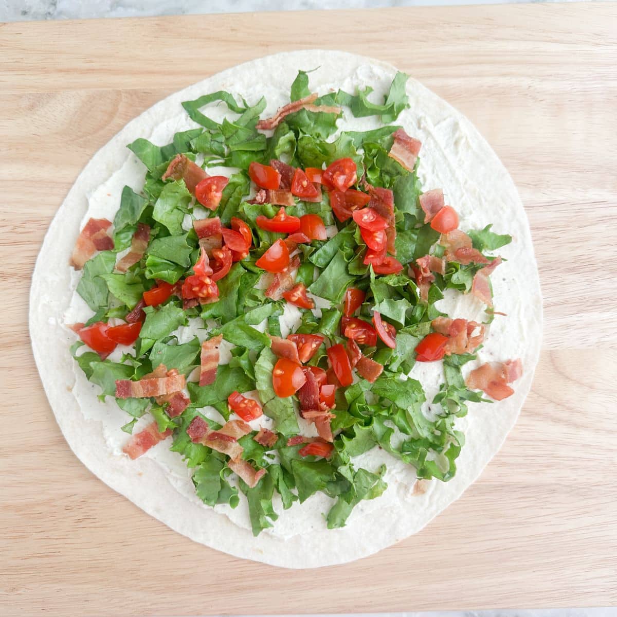 Tortilla topped with cream cheese, lettuce, crumbled bacon, and tomatoes.