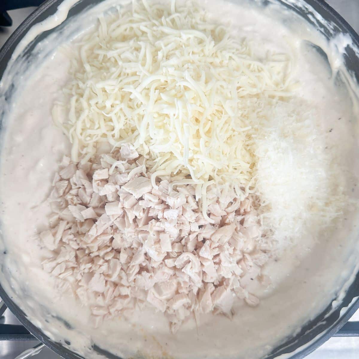 Saucepan with melted cream cheese, shredded chicken, and shredded cheese.