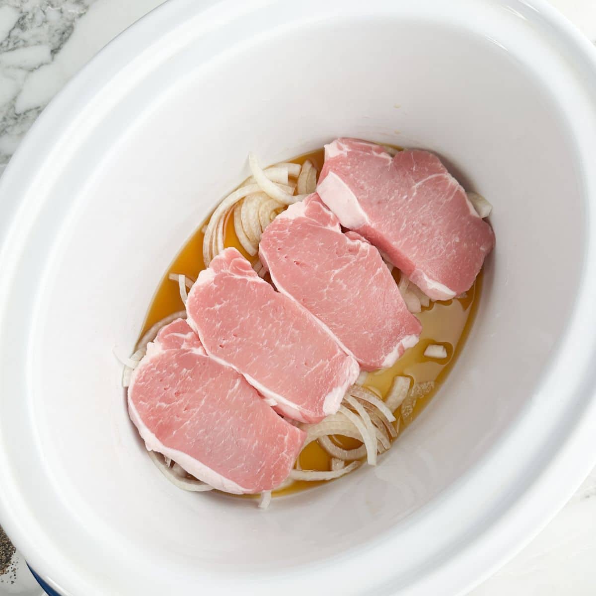 Slow cooker with broth, onions, and pork chops.