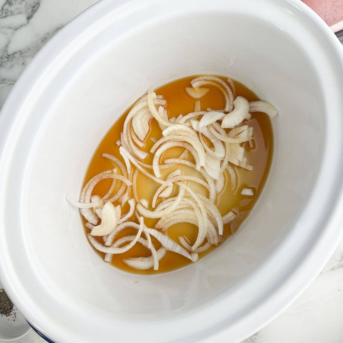 Slow cooker with beef broth and sliced onions.
