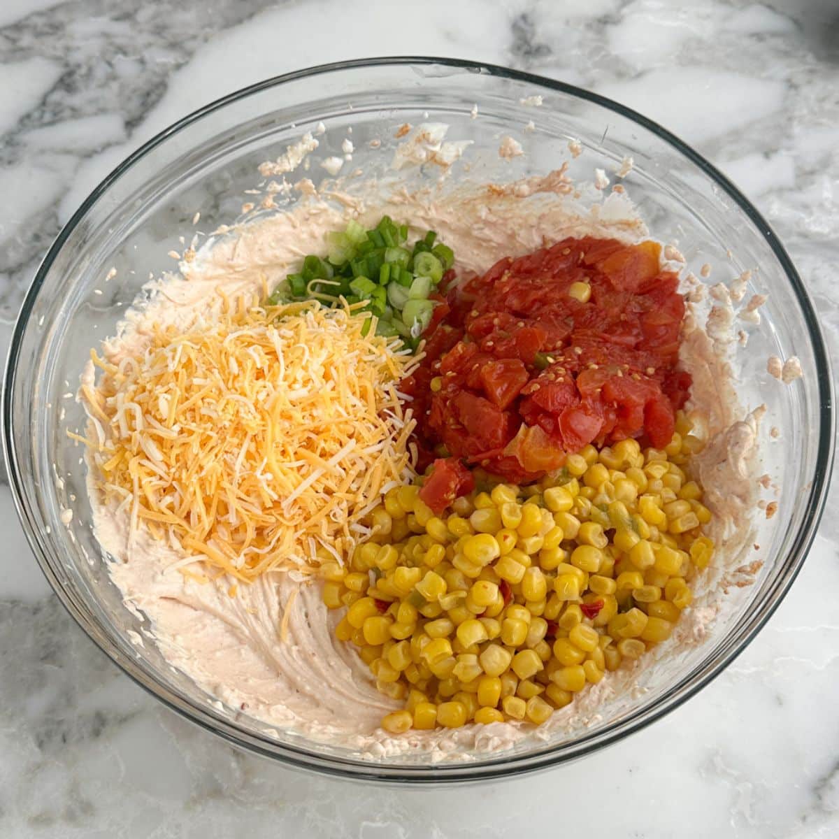 Bowl of creamy dip with shredded cheese, corn, and Rotel tomatoes.