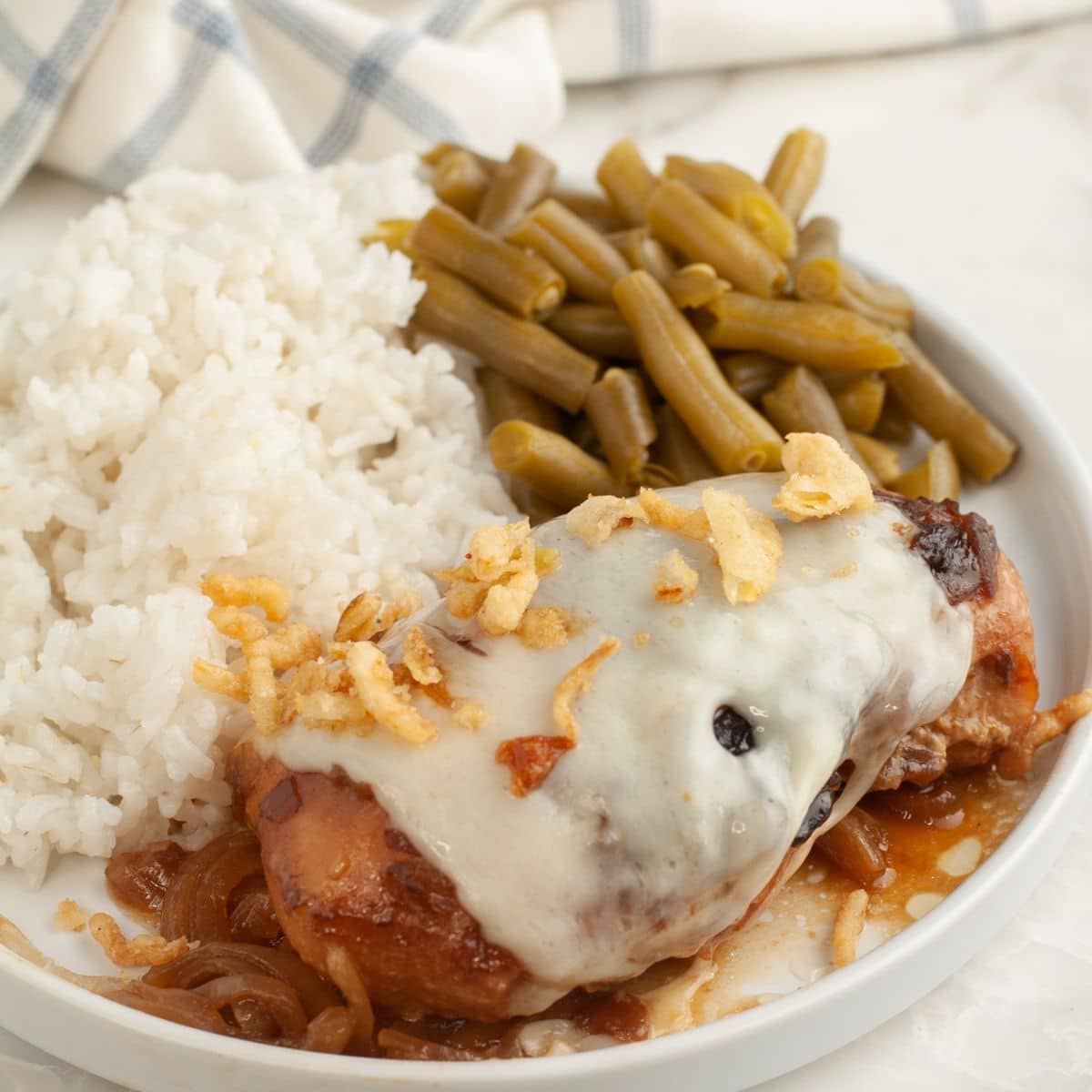 Plate with chicken topped with Swiss cheese, rice, and green beans.