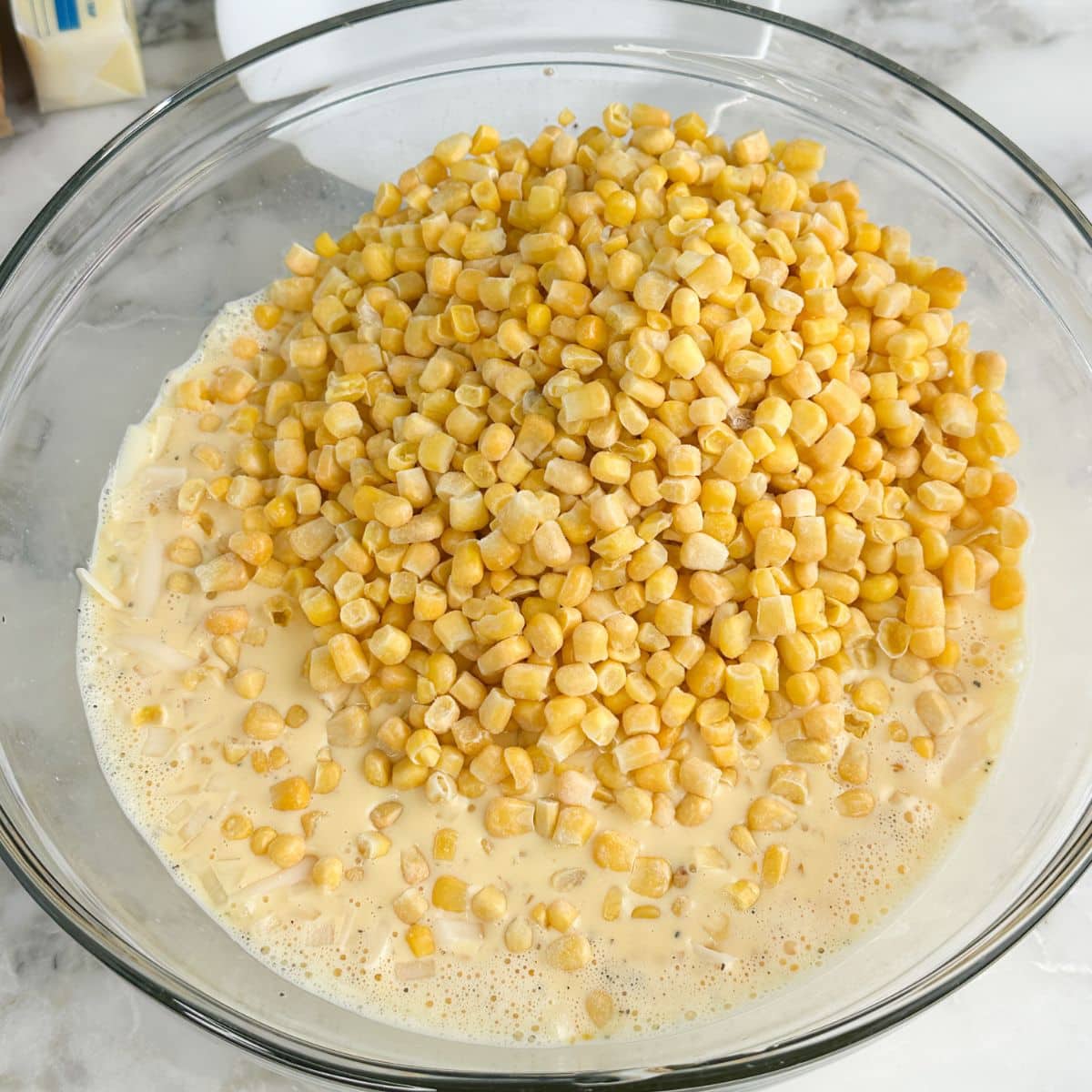 Bowl of beaten eggs, milk, and corn.