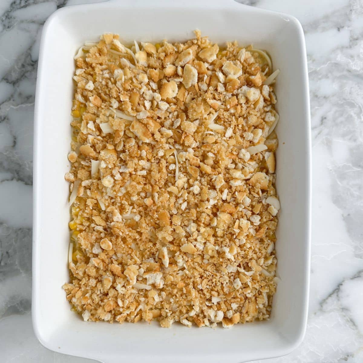 Baking dish with corn casserole topped with crumbled crackers. 