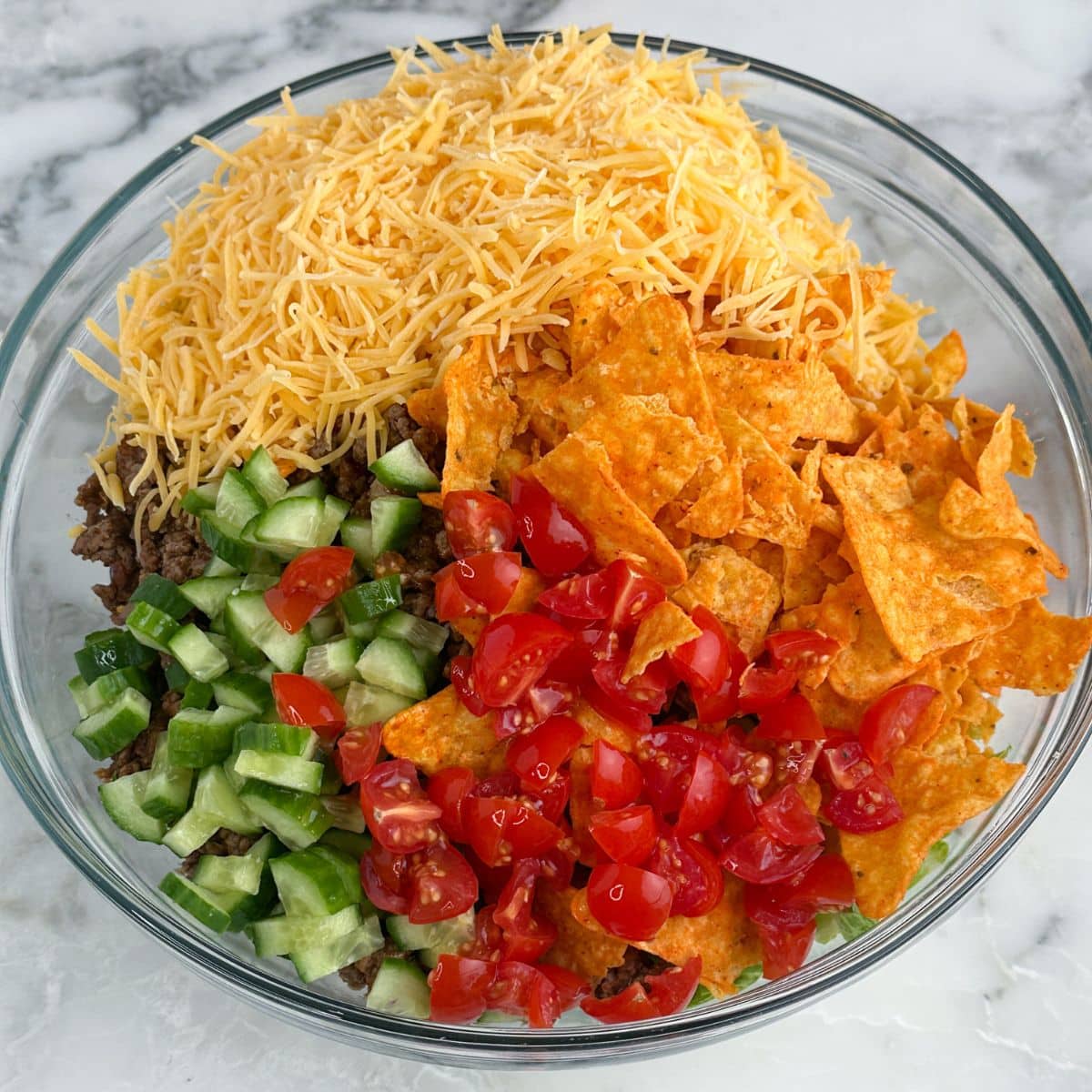 Bowl of shredded cheese, Doritos, diced cucumbers, and tomatoes.