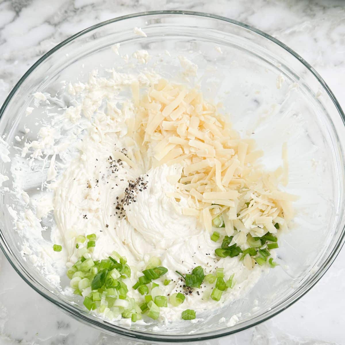 Bowl of cream cheese, shredded cheese, and diced green onion. 
