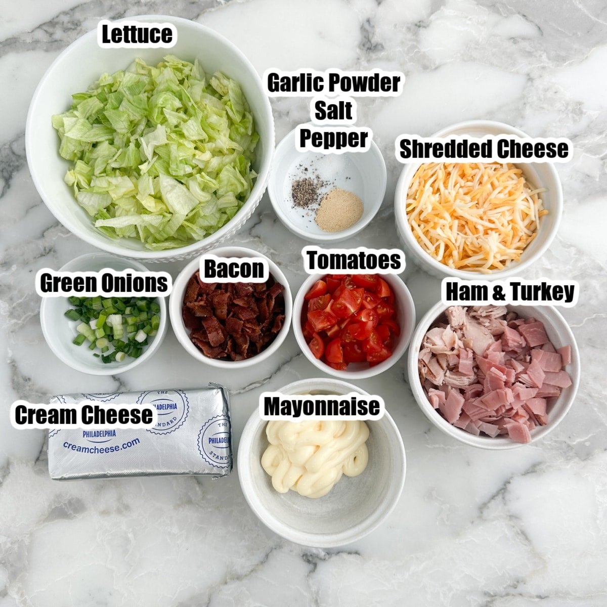 Bowl of chopped lettuce, tomato, green onions, shredded cheese, mayonnaise, bacon, seasonings, and mayonnaise.