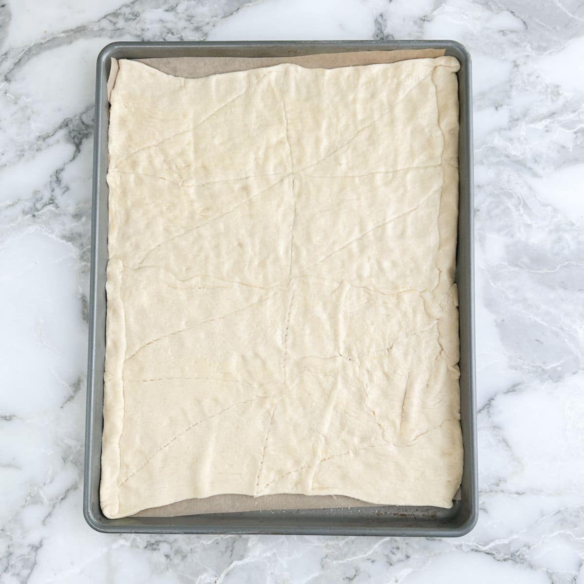 Baking pan with uncooked crescent roll dough spread out. 
