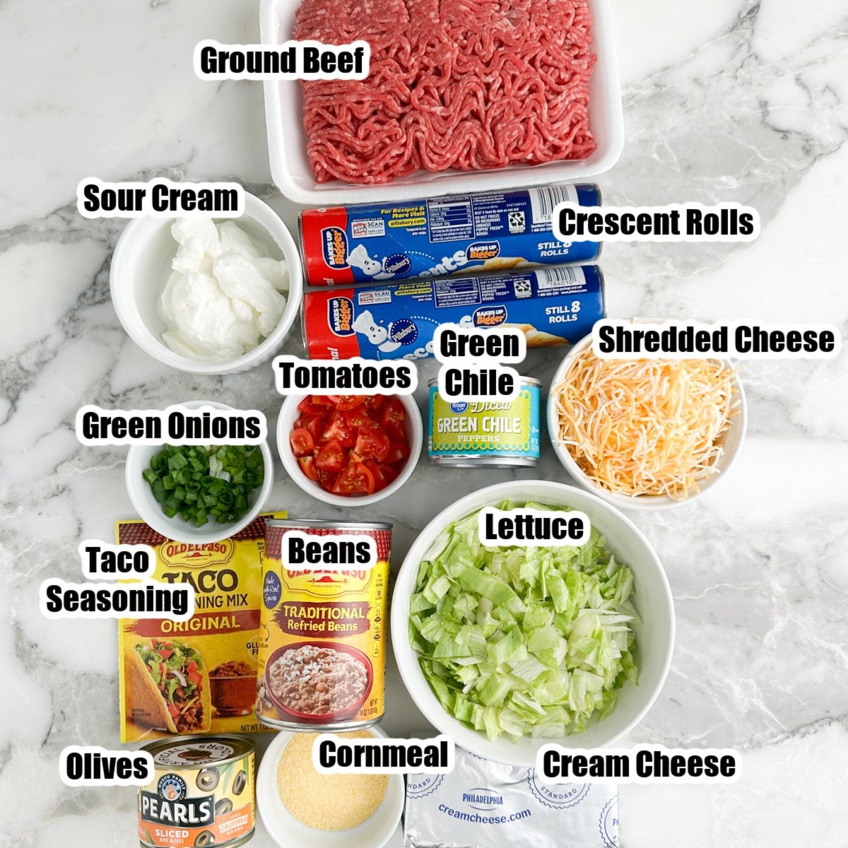 Ground beef, can of crescent rolls, bowl of cheese, sour cream, tomatoes, onion, lettuce, can of beans, and taco seasoning. 